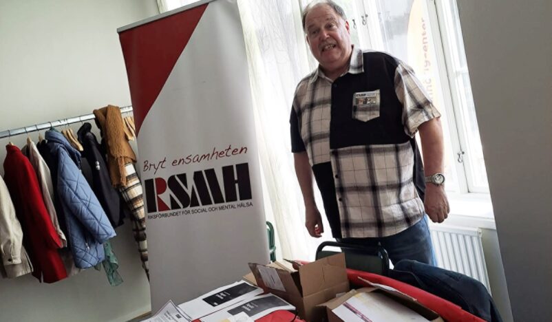 Stefan Wallerek i rutig skjorta vid bord med RSMH-broschyrer
